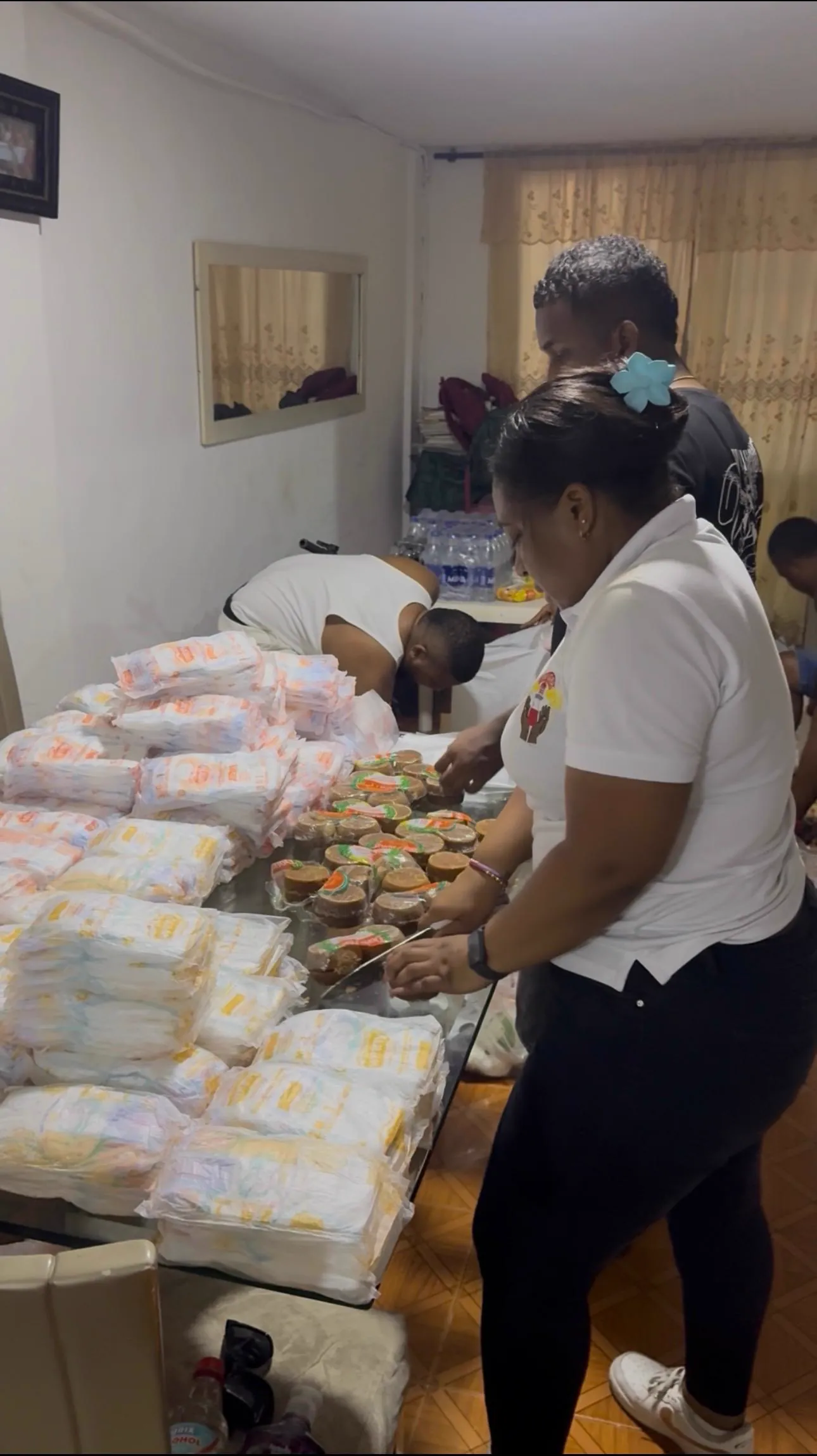 Voluntarias con camiseta blanca empacan pañales y alimentos sobre una mesa para completar las remesas