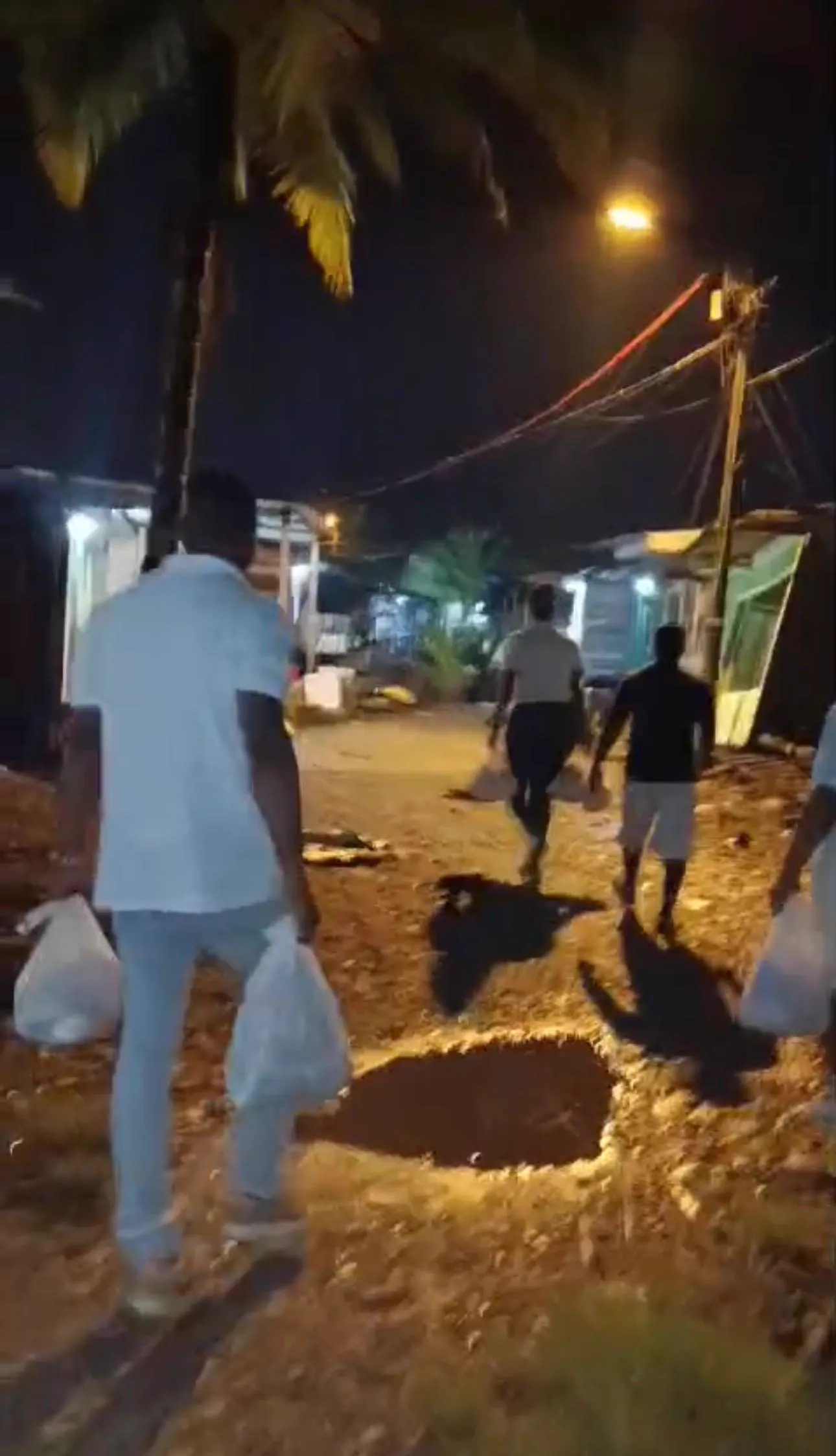 Voluntarios caminan de noche por una calle destapada cargando bolsas con ayuda humanitaria